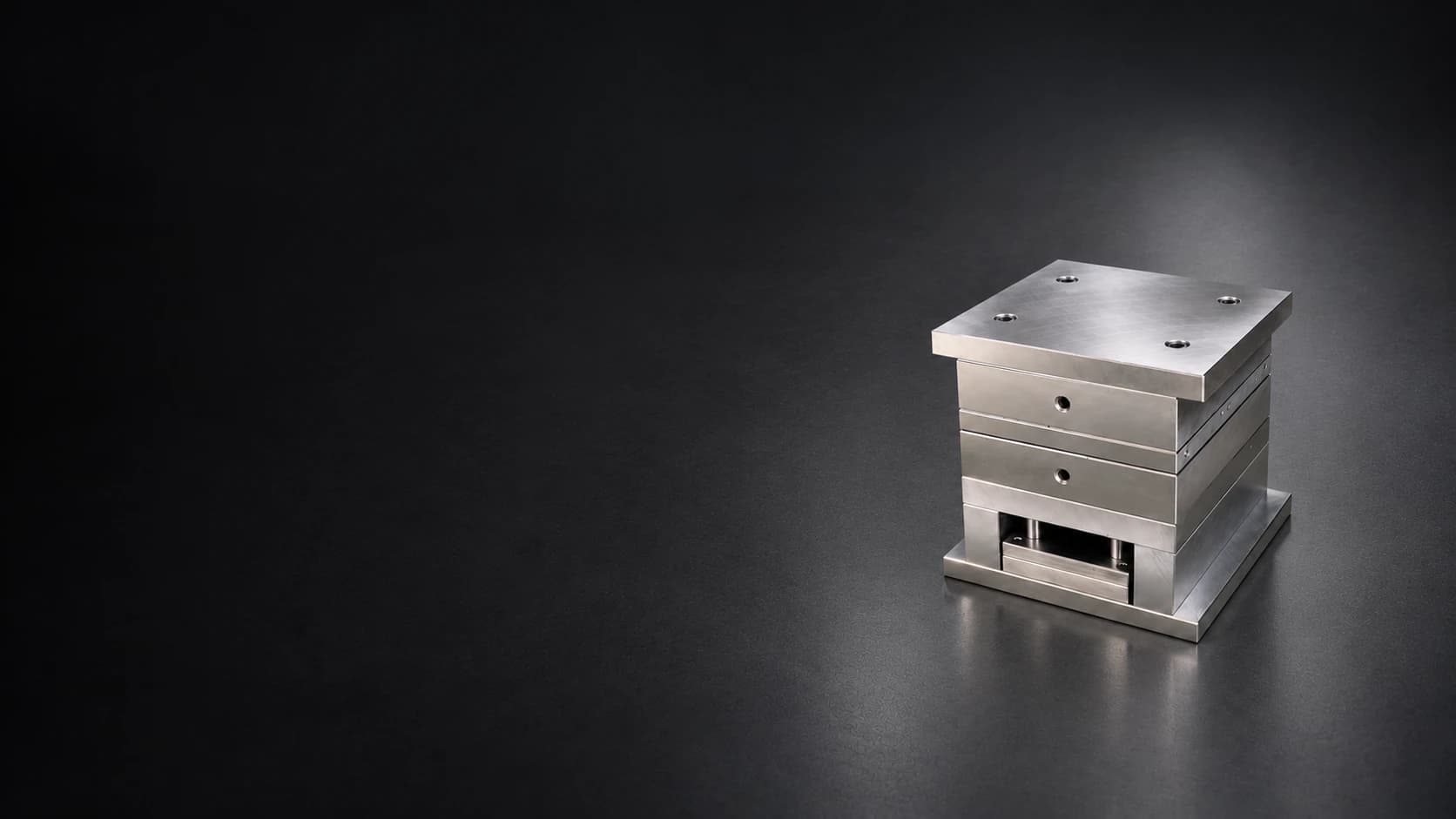 Assembled steel mold base with aligned plates and a lower ejector assembly on a dark charcoal floor